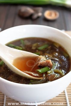 a white bowl filled with soup sitting on top of a wooden table next to green beans