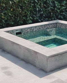 an outdoor hot tub in the middle of a patio with green plants behind it,