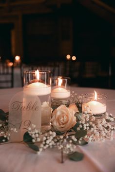 candles are lit on a table with flowers and greenery