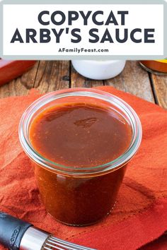 a glass jar filled with bbq sauce on top of a red napkin next to a fork