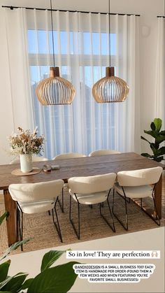 a dining room table with white chairs and two hanging lights over the top of it