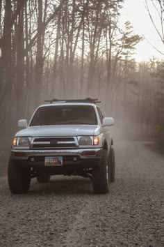 a silver truck driving down a dirt road next to trees in the foggy forest