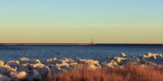 there is a lighthouse in the distance near some rocks and grass on the shore line