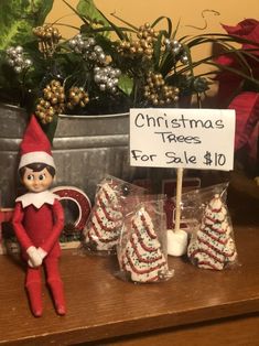 an elf is sitting on a table with christmas trees for sale in front of him