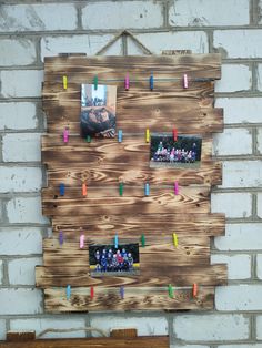 a wooden wall hanging on the side of a brick building with photos pinned to it