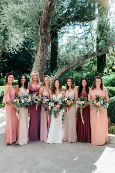 a group of women standing next to each other holding bouquets in front of a tree