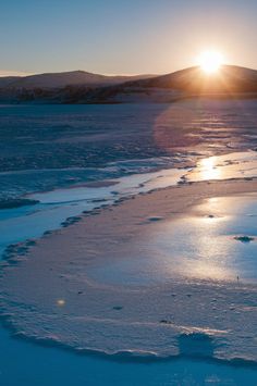 the sun is setting over an icy lake with ice and snow flakes on it