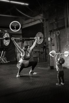 a woman holding a barbell while standing next to a child