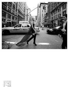 a woman walking across a street next to tall buildings