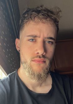 a close up of a person with a beard wearing a black shirt and looking at the camera