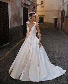 a woman in a white wedding dress standing on the side of an alleyway with buildings behind her