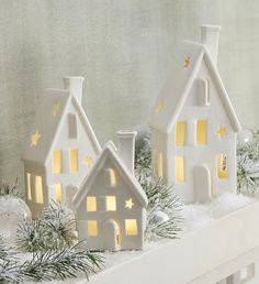 three small white houses are sitting on a mantle with snow and pine branches in front of them