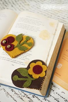 an open book with two felt flowers on it and a button in the shape of a heart