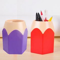 two vases with pencils and markers in them sitting on a wooden table next to each other