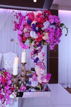 a tall vase filled with lots of purple and pink flowers next to two lit candles