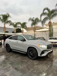 a white mercedes gle is parked in front of some palm trees and other cars