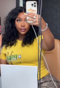 a woman sitting in front of a laptop computer holding a cell phone up to her face