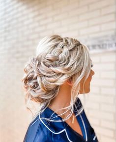 a woman with blonde hair wearing a blue dress and braided updo is standing in front of a brick wall