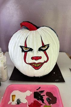 a white pumpkin with red and black paint on it sitting next to a pink tray