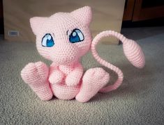 a crocheted pink cat sitting on the floor with blue eyes and tail,