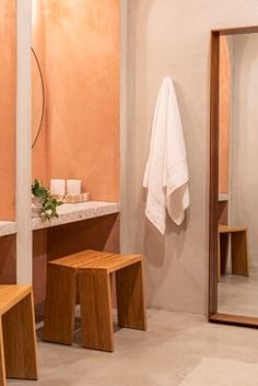 a bathroom with two wooden stools and a large mirror in the wall next to it