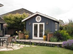 a backyard with a table and chairs in the grass next to a blue shed that has flowers on it