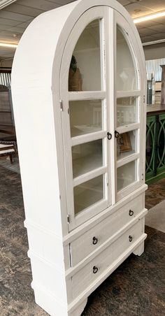 a white china cabinet with glass doors on the top and bottom shelves, in a store