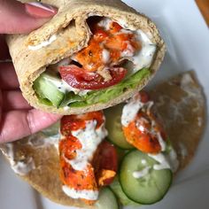 a hand holding a pita filled with meat and veggies next to cucumbers