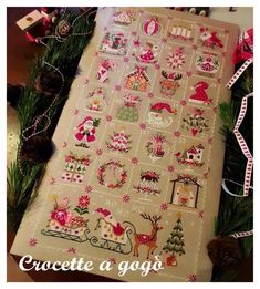 a cross stitch pattern on a table next to some christmas decorations and pine cones with ribbons