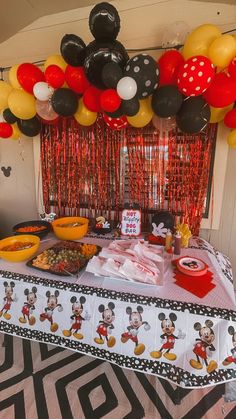 a mickey mouse themed birthday party with balloons and streamers on the ceiling, table