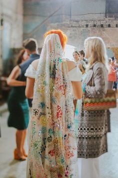 two women standing next to each other in front of a group of people wearing colorful clothing