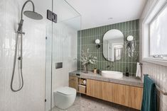 a bathroom with green tiled walls and white fixtures on the vanity, toilet and shower