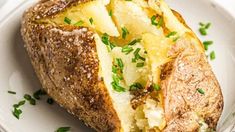 a baked potato on a white plate topped with parmesan cheese and chives