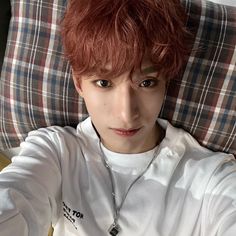 a man with red hair sitting on top of a couch wearing a white shirt and silver necklace