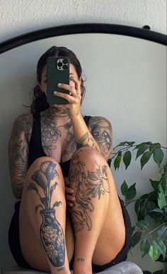 a woman with tattoos taking a selfie in front of a mirror while sitting on a bed