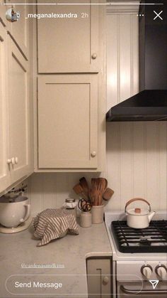 a kitchen with white cupboards and an oven in the corner, next to a tea kettle