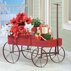 a red wagon filled with presents on top of snow covered ground next to a house