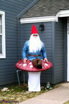 a man dressed as a gnome is standing in front of a house with a mushroom hat on