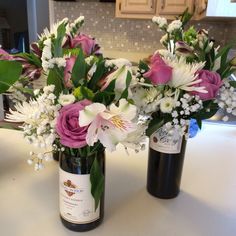 two wine bottles with flowers in them sitting on a counter