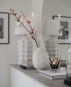 two white vases with flowers in them sitting on a table next to a mirror