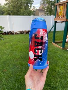 a hand holding up a blue and red soda can in front of a swing set