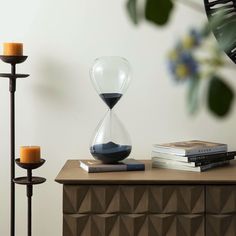 an hourglass sitting on top of a wooden table next to two candles and books