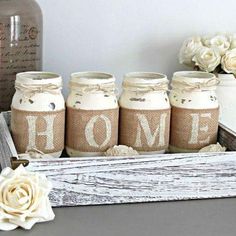 four jars with the word home are sitting on a table next to flowers and vases