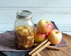 apples and cinnamon sticks sit on a cutting board next to a jar of apple cider