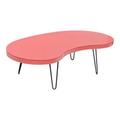 a pink coffee table with black hairpinks on the legs and an oval shaped top