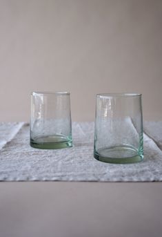 two empty glasses sitting on top of a white cloth covered placemat with a gray background