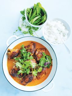 a white bowl filled with meat and greens next to some other food on a blue surface