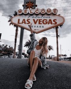 a woman sitting in front of the welcome to fabulous las vegas sign with her legs up