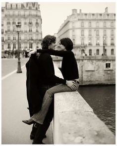 black and white photograph of two people sitting on a wall kissing each other in paris