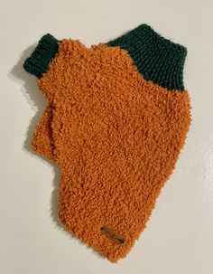 an orange and green knitted mitt laying on top of a white tablecloth